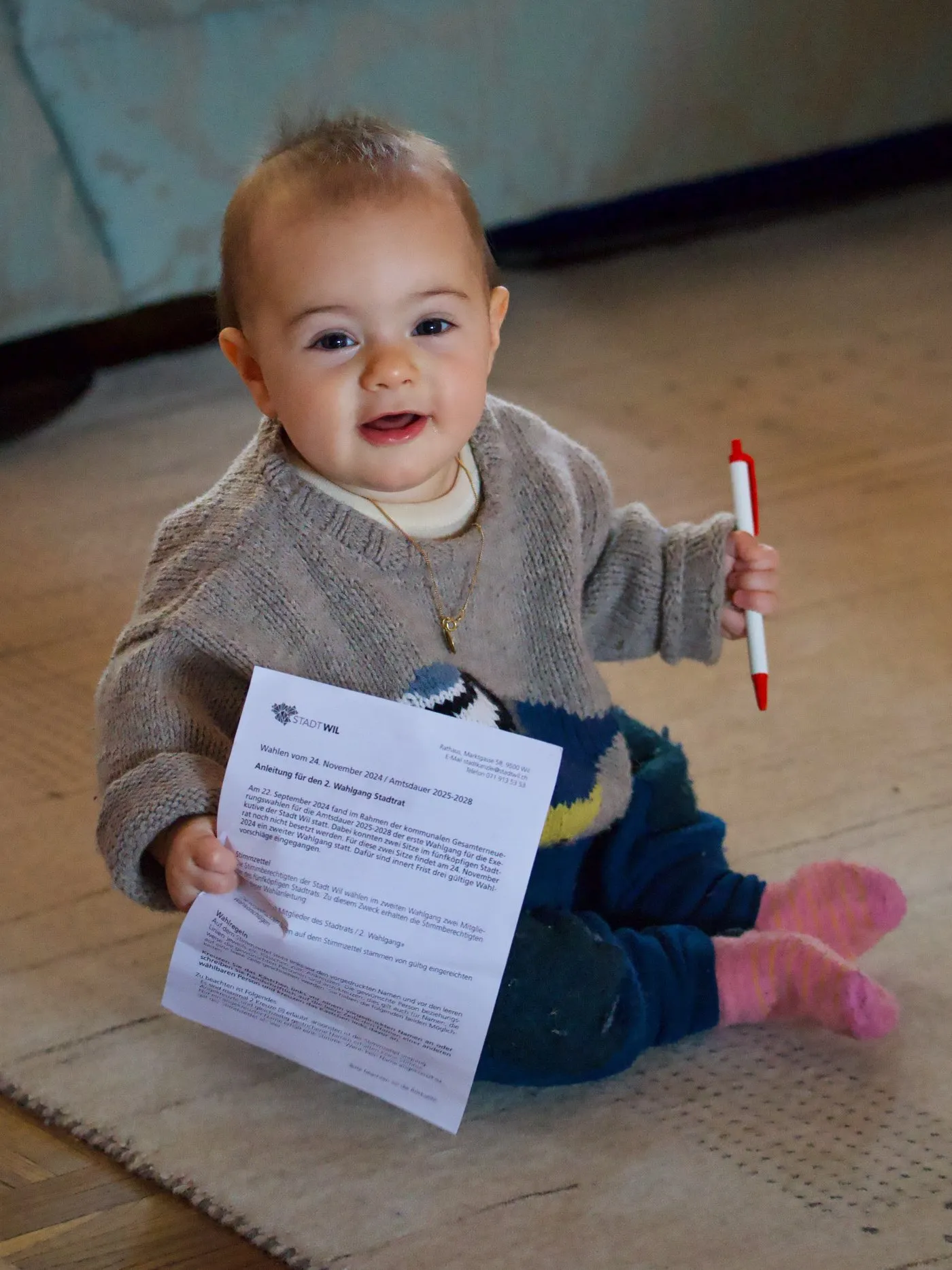 Baby sitzt am Boden und hält ein Formular und einen Kugelschreiber
